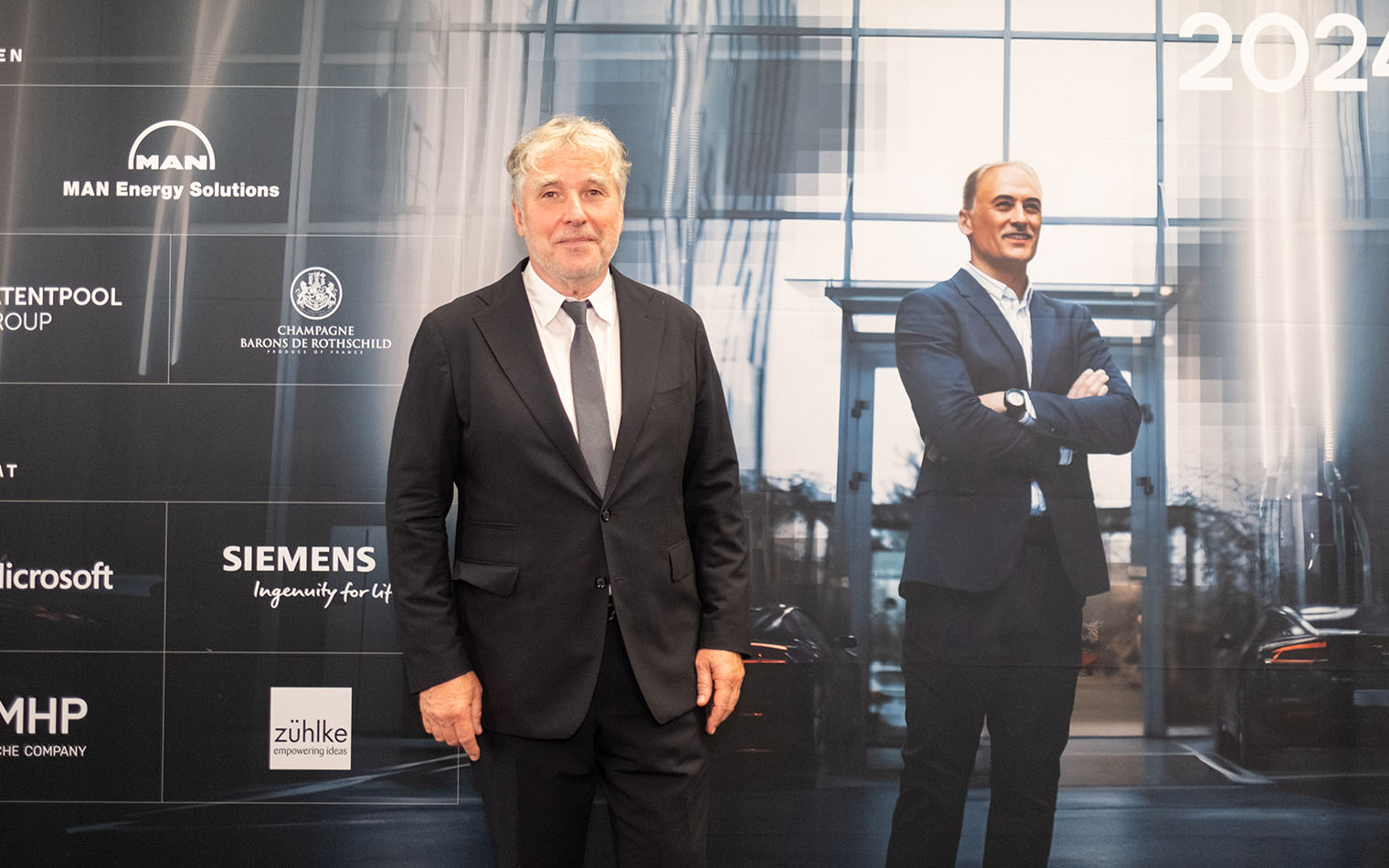 Prof. Kurt Mehnert in front of the sponsor wall of the Diesel Medal 2024.